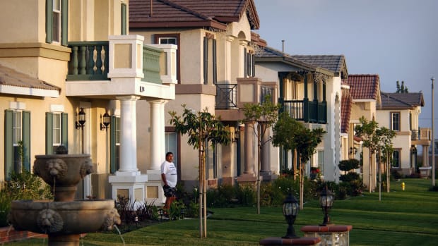 A man is seen standing in front of a house in a row of them. -lead