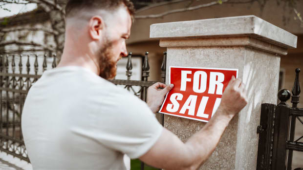 A man puts a "for sale" sign on his home. -lead