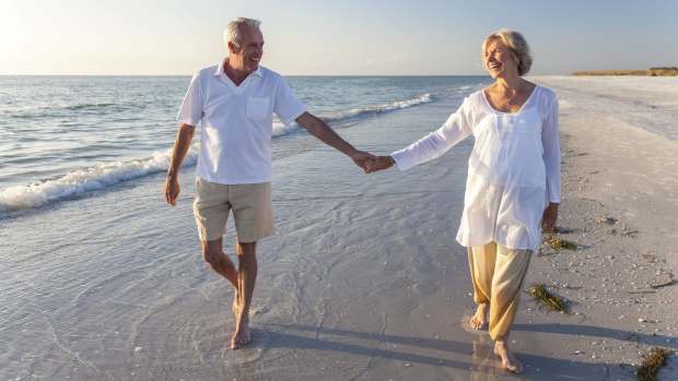 A retired couple is seen holding hands and walking on a beach. -lead