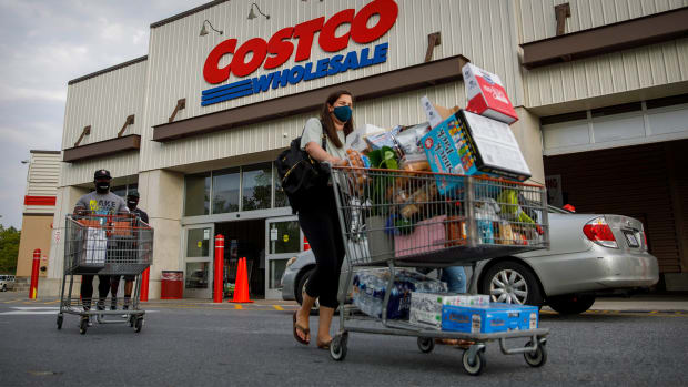 A woman pushes a packed cart out of Costco. Lead.