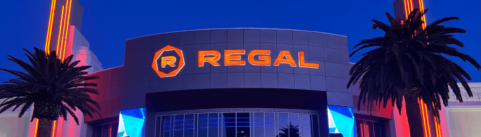 Wide, thin photo of the top of a Regal Cinemas building at night with the "Regal" name and logo visible in the center